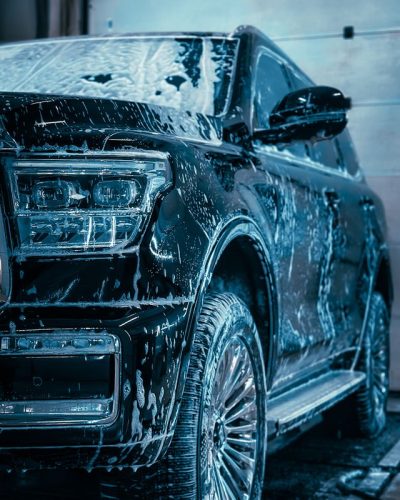 Close-up of a sleek SUV covered in soap during a car wash, highlighting cleanliness and care.