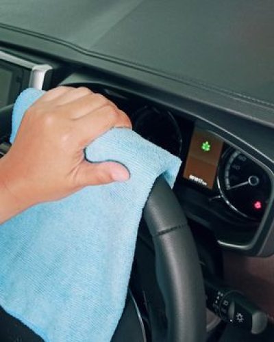 From above crop unrecognizable person polishing modern car steering wheel with blue fiber cloth