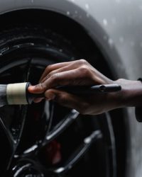A detail-oriented close-up of a hand cleaning a car tire with a brush and soap.