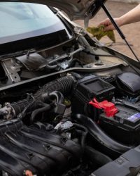 Mechanic inspecting car engine bay and battery during routine maintenance.